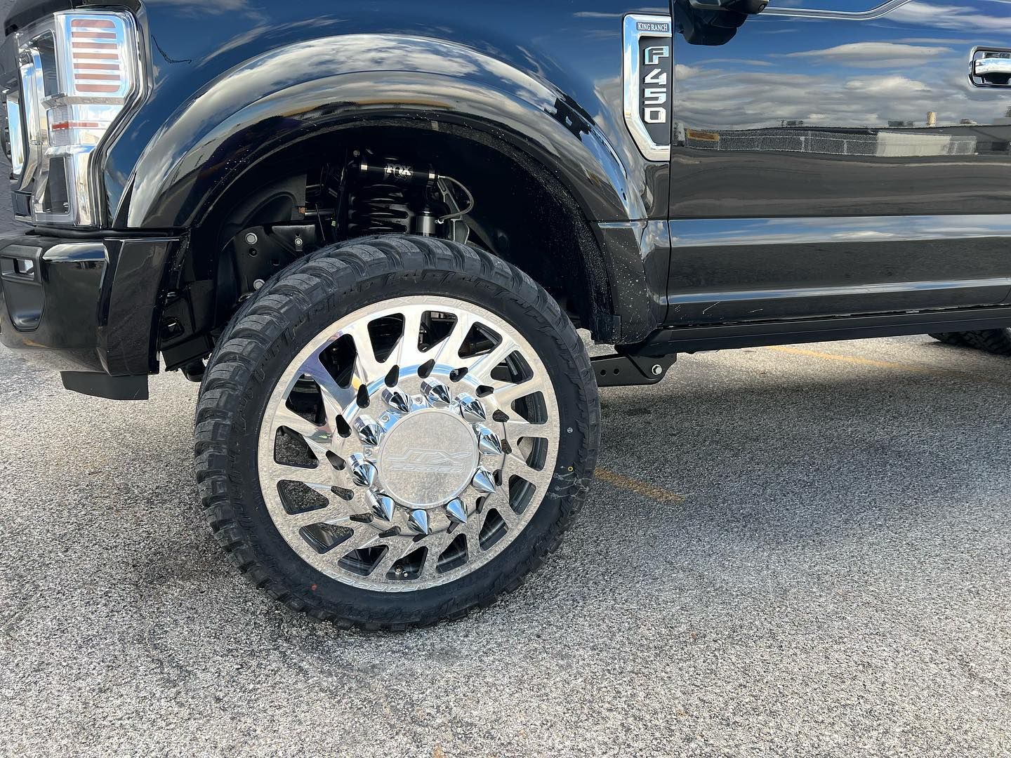 Close-up of a black pickup truck’s front wheel with a chrome rim on a gravel surface