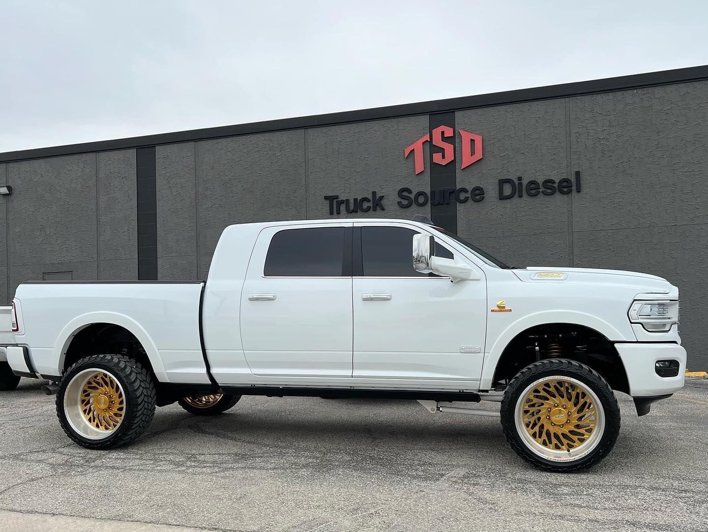White lifted pickup truck with gold wheels parked outside Truck Source Diesel.