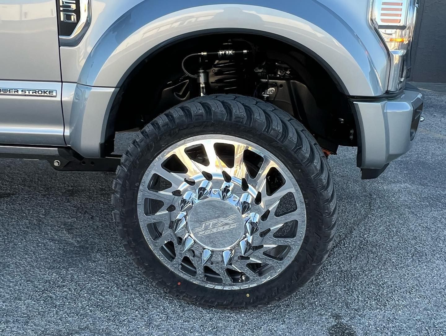 Silver truck front wheel with chrome rim and off-road tire on pavement