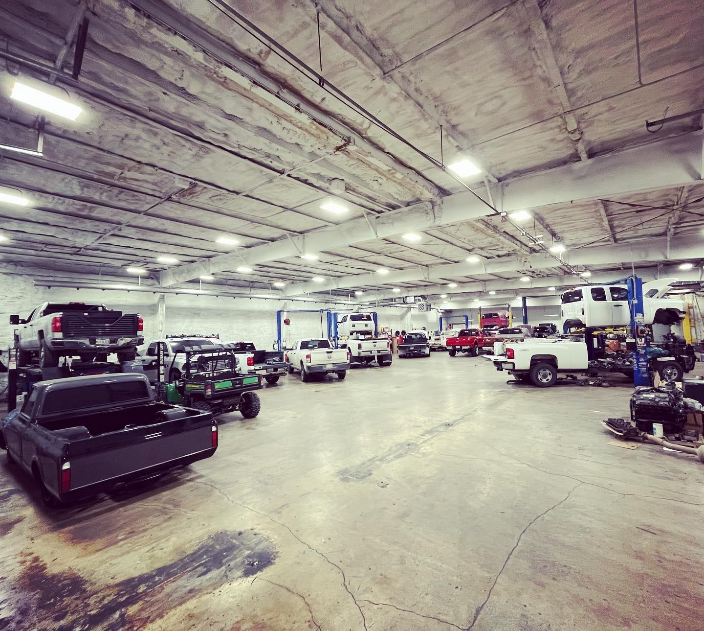 Large indoor garage with multiple utility vehicles, equipment, and fluorescent ceiling lights.