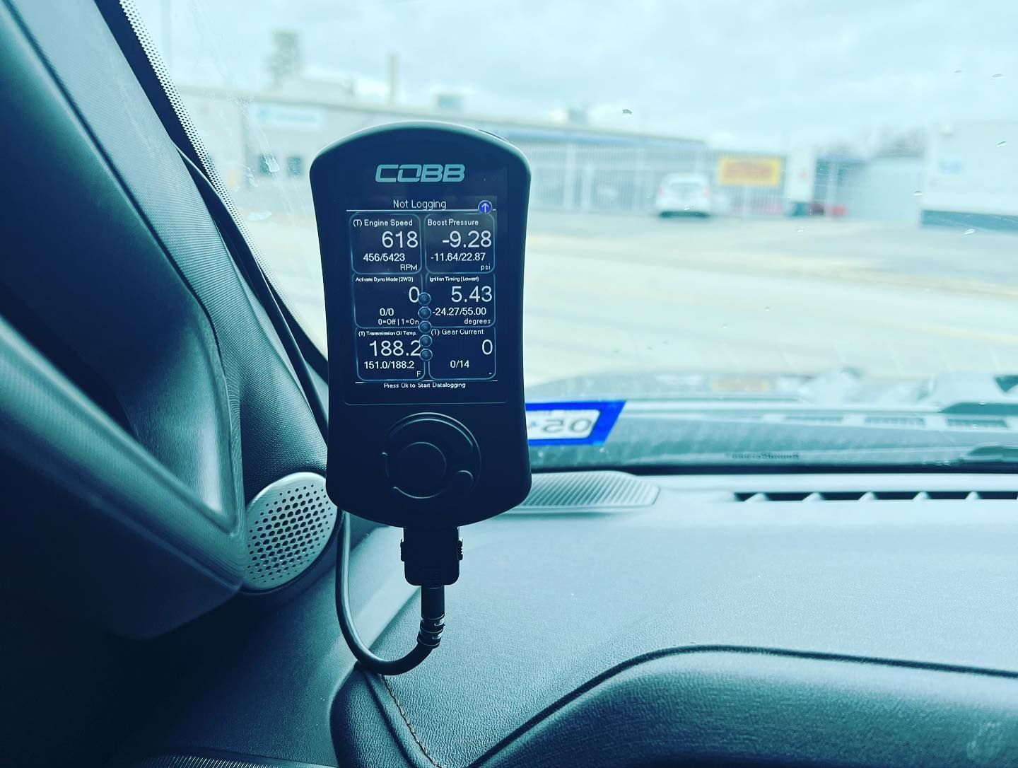 Black COBB tuner mounted on a car dashboard, with a road visible through the windshield.