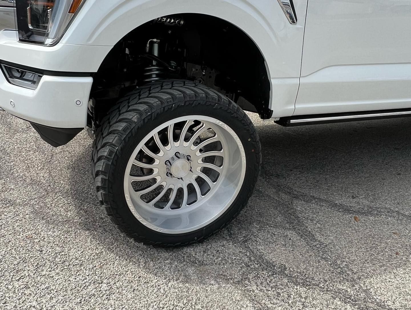 White lifted truck with large off-road wheel parked on pavement
