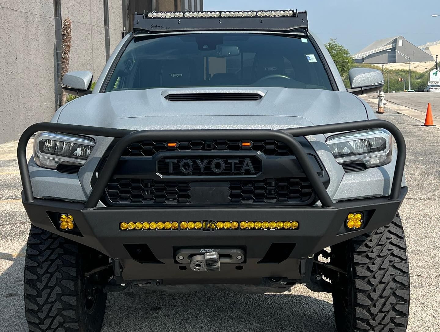 Front view of a gray Toyota off-road truck with a lift, heavy bumper, and roof light bar.