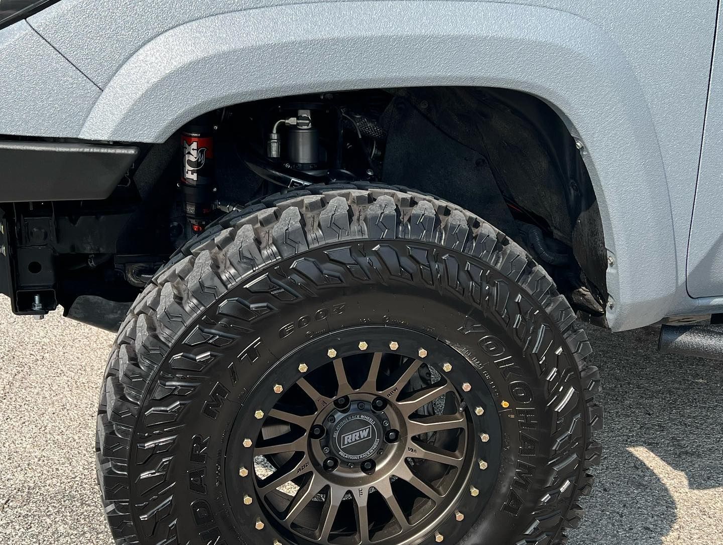 Silver truck with black off-road wheel and tire under a fender on pavement