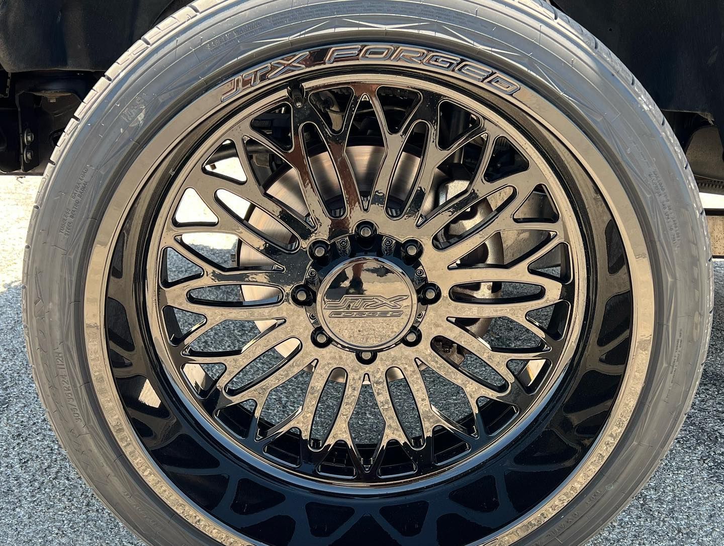 Black custom car wheel with intricate spoke design and low-profile tire on a vehicle.