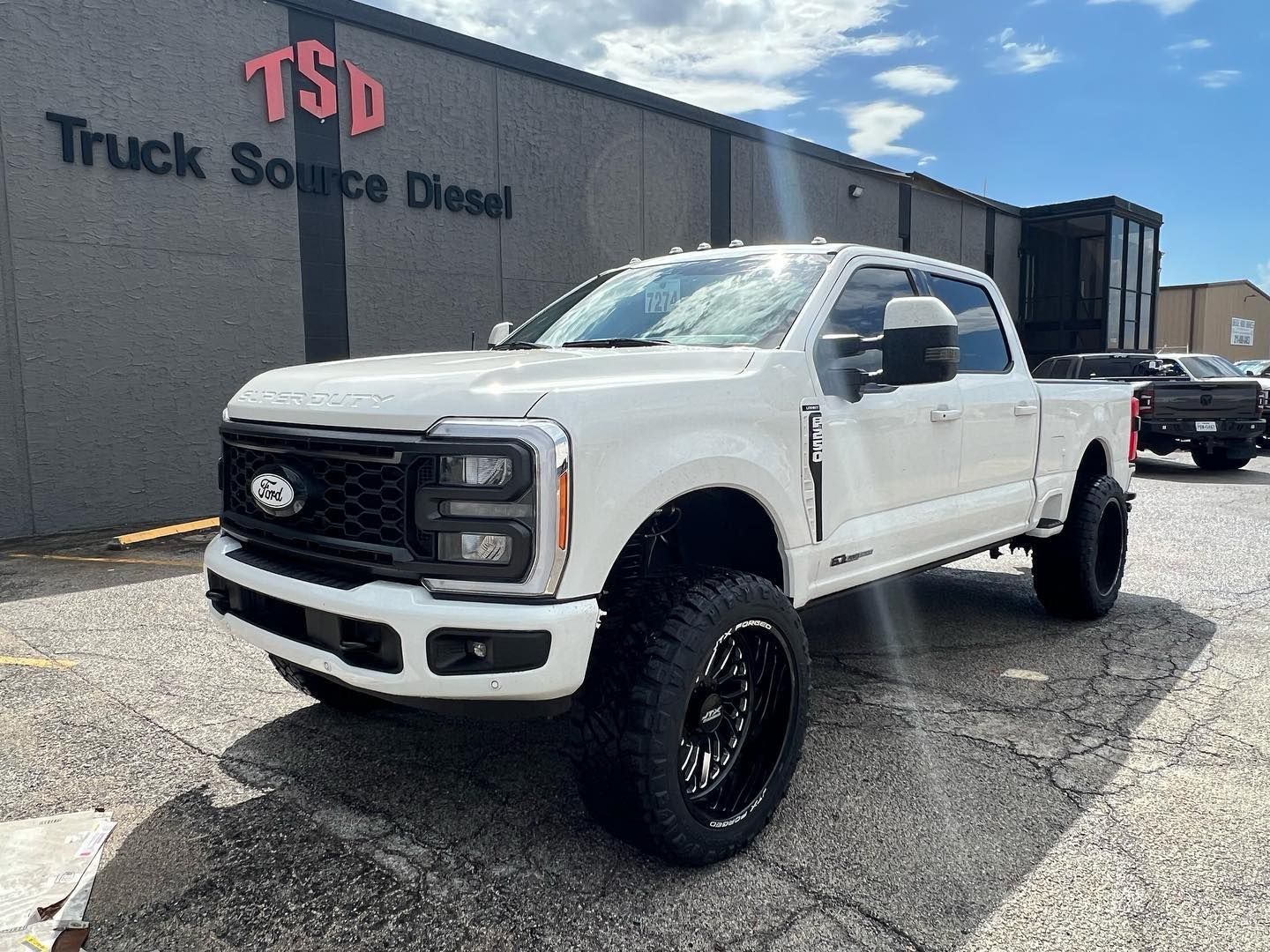 Lifted white Ford truck parked outside a diesel shop under a blue sky.