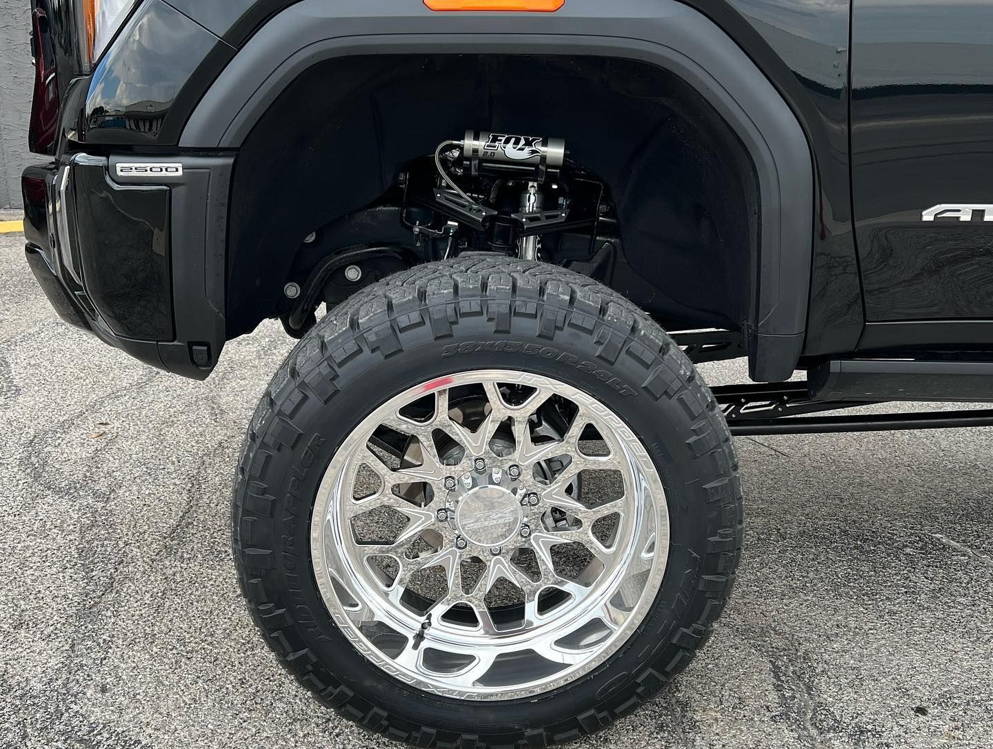 Black truck with a large chrome wheel and off-road tire on a gravel surface