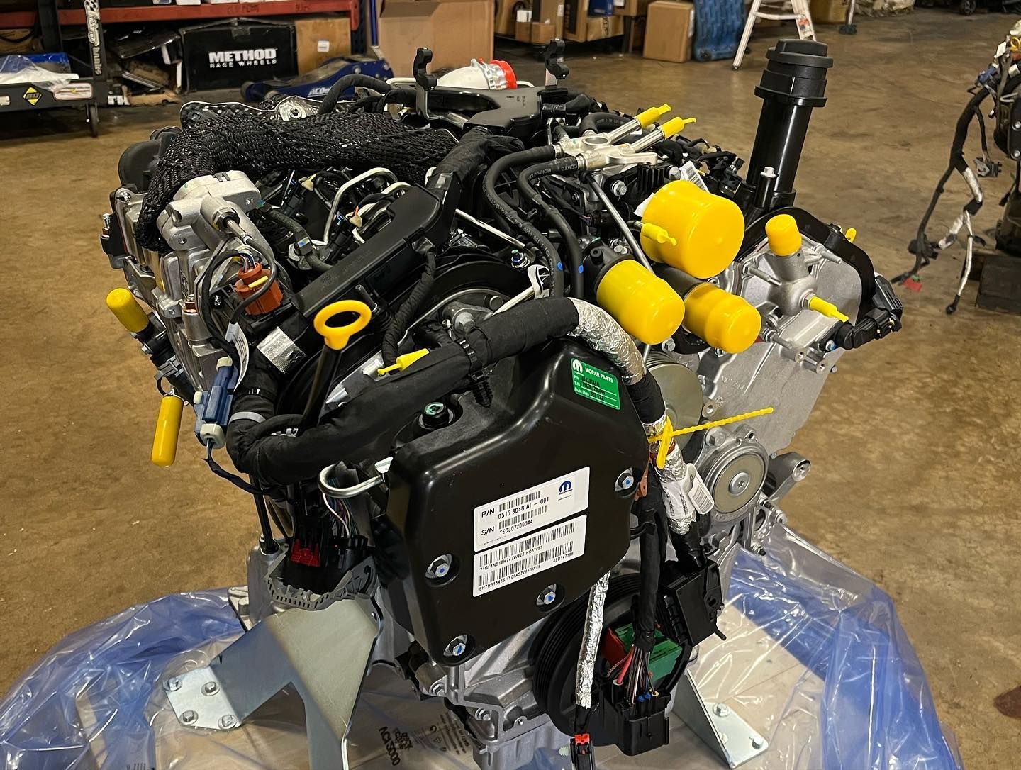 Large black engine or machine assembly wrapped in plastic, with yellow caps, in a workshop.