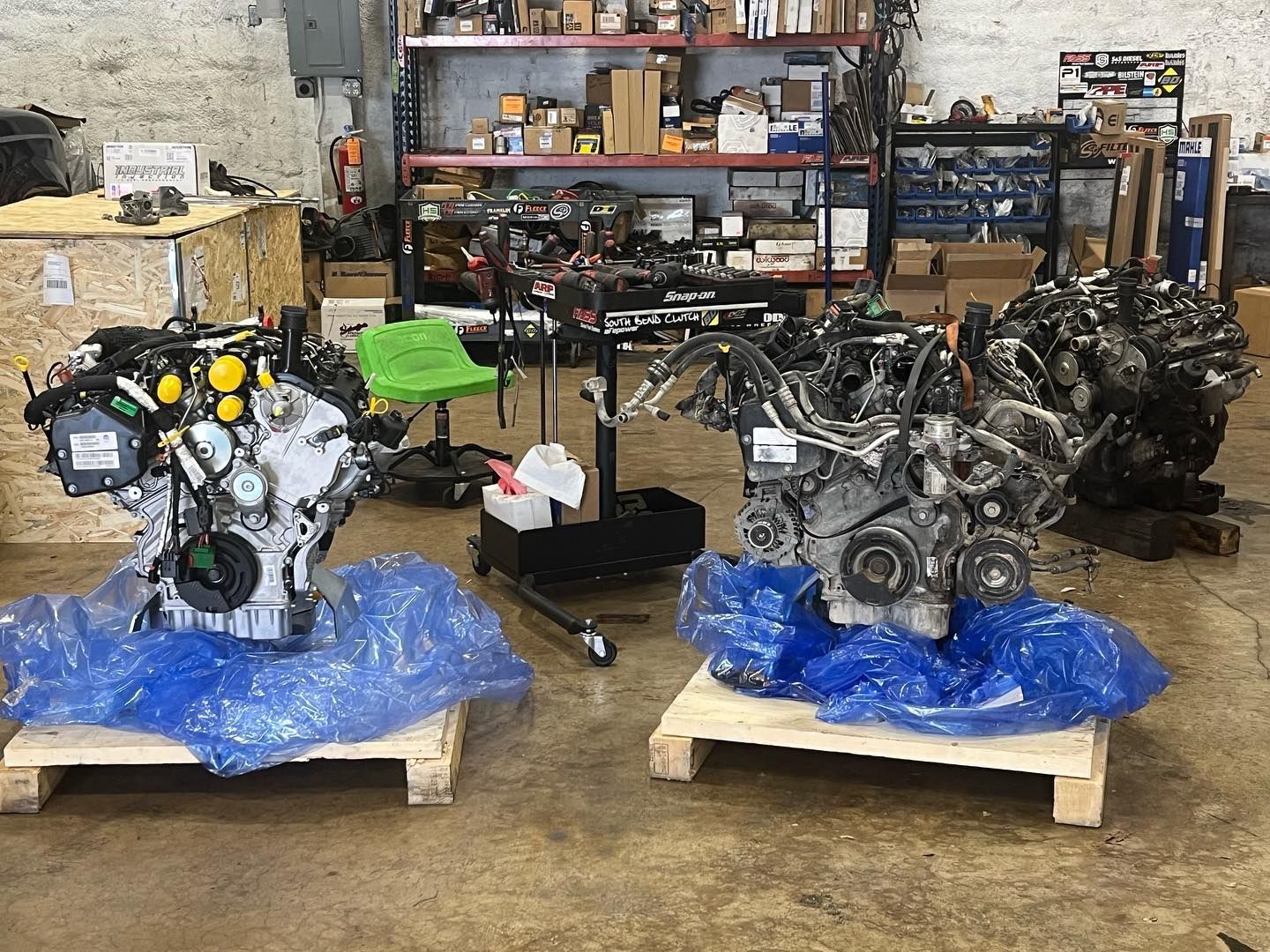Two engine assemblies on blue tarps in a workshop, with shelves and tools in the background
