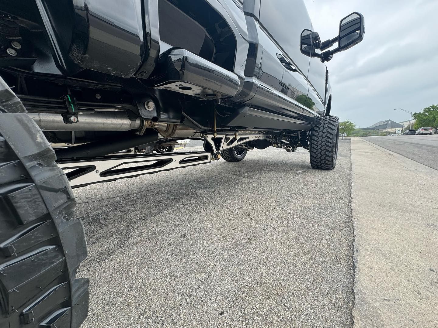 Low-angle view of a black lifted truck parked on a roadside under a cloudy sky.