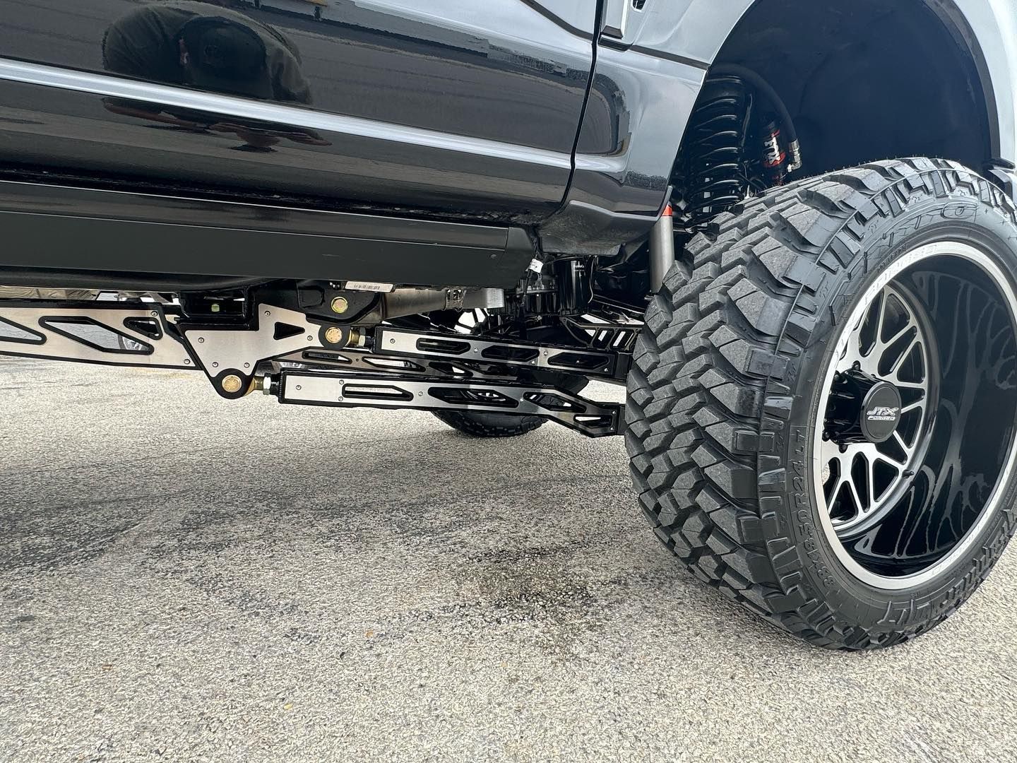 Black lifted truck with oversized off-road tires parked on pavement, side view