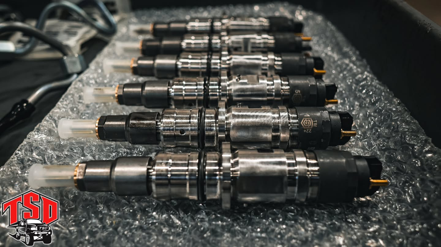Rows of shiny metal mechanical parts laid out on bubble wrap, with black cables in the background.