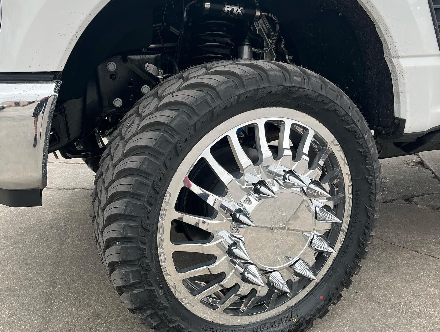 Chrome truck wheel with chrome rims and off-road tire under a white fender