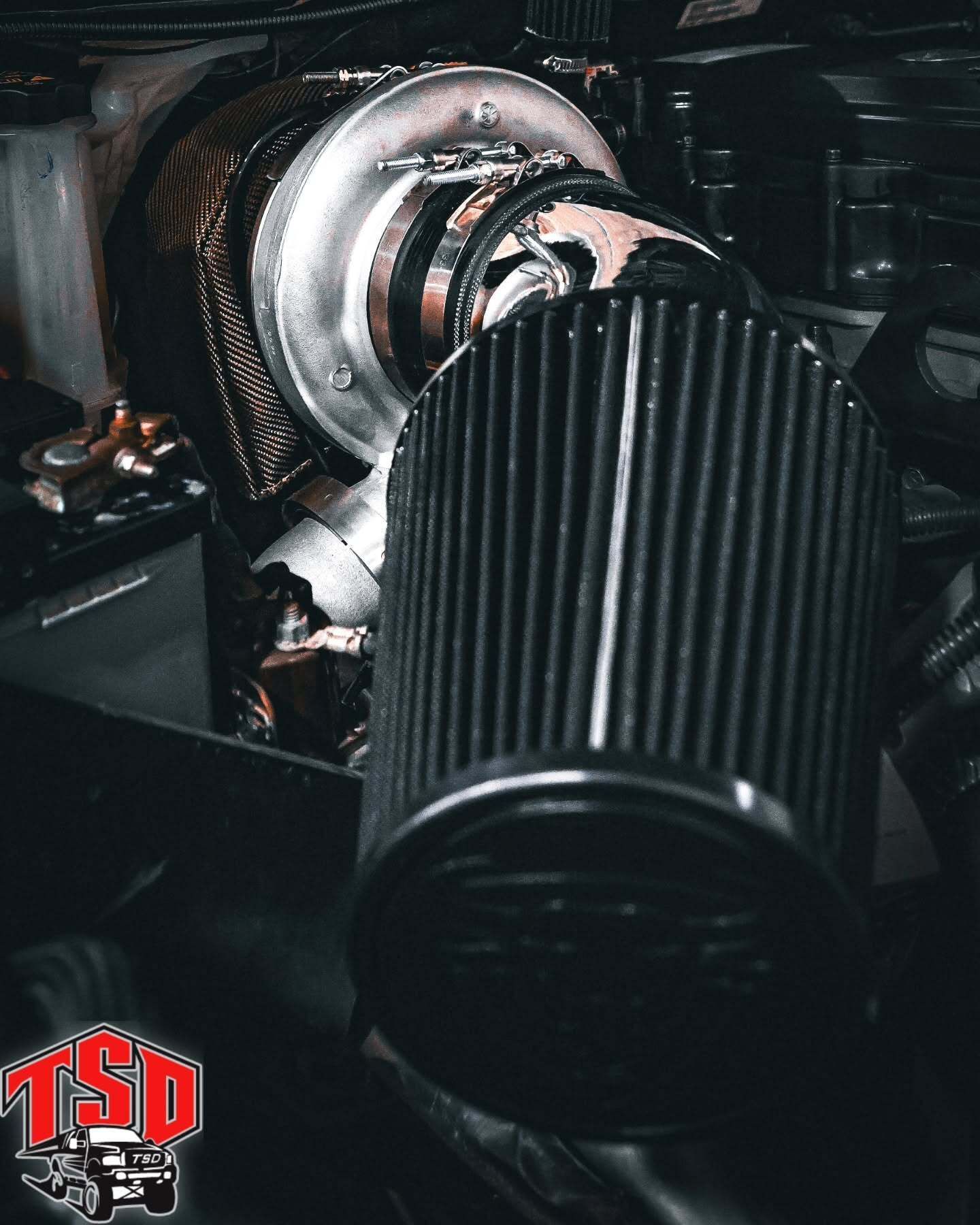 Close-up of a car engine with a black cone air filter and polished turbocharger