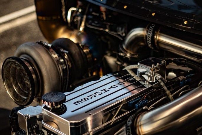 Close-up of a polished car engine with a silver valve cover and turbocharger in a dark engine bay
