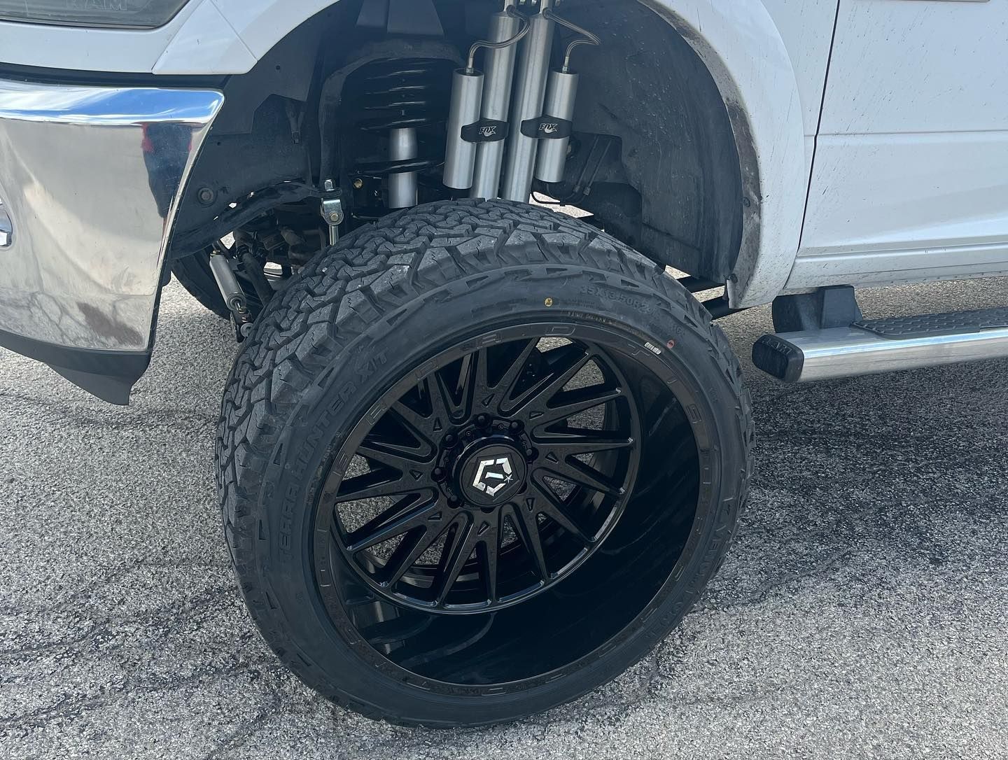 Black off-road wheel on a lifted truck, showing suspension in a parking lot