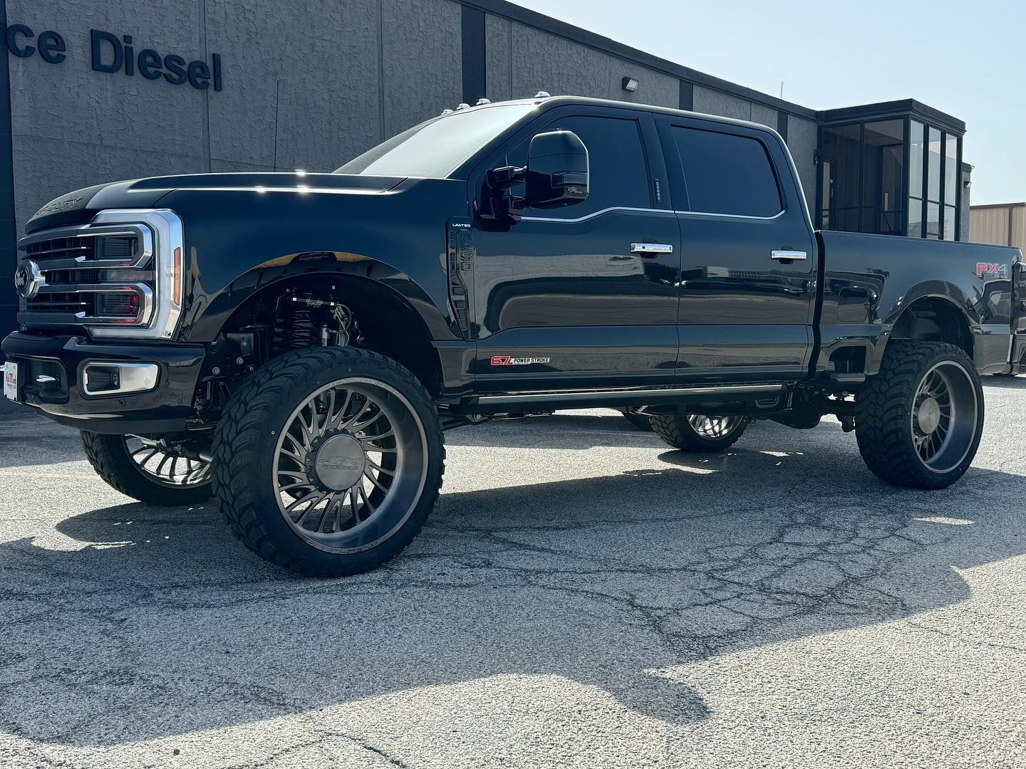 Lifted black pickup truck parked outdoors on gravel in front of a building.
