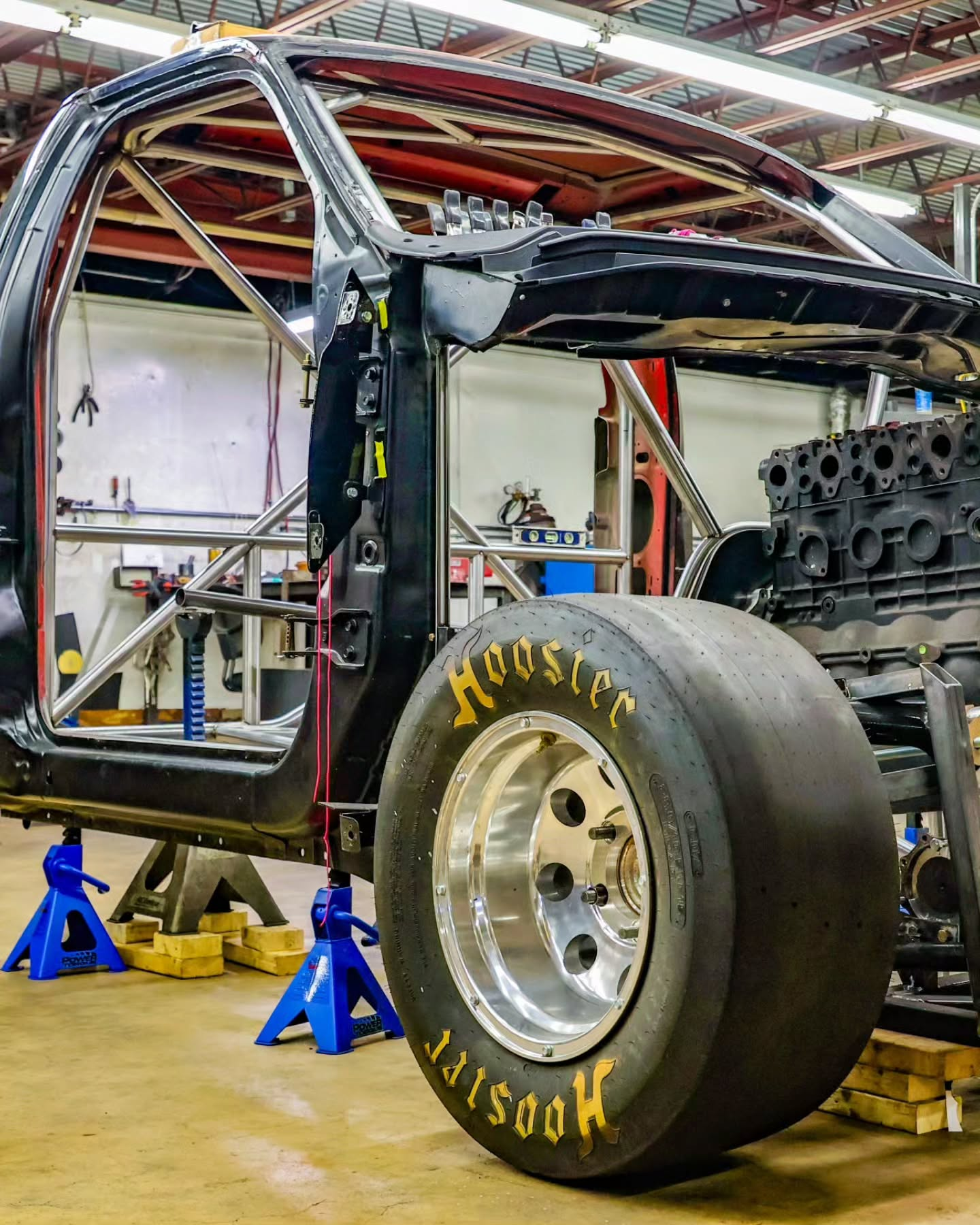 Racing car chassis on jack stands in a garage, with large rear tire and exposed engine components