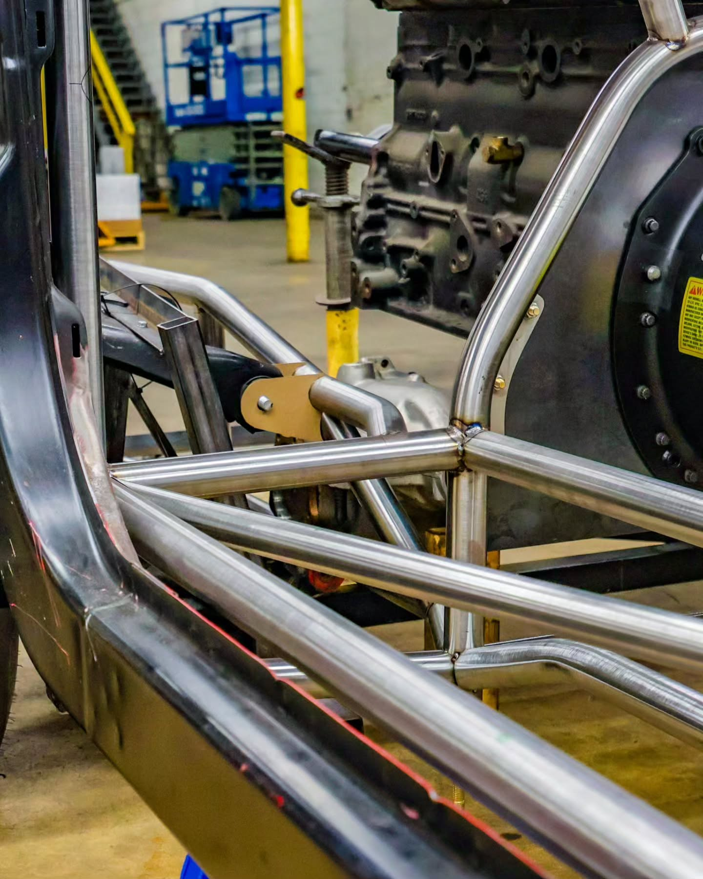 Metal tubing and vehicle chassis frame in a workshop, with industrial machinery in the background