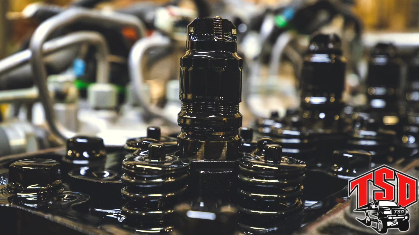 Black oil nozzles and machinery parts in a factory, with a red TSD logo in the corner