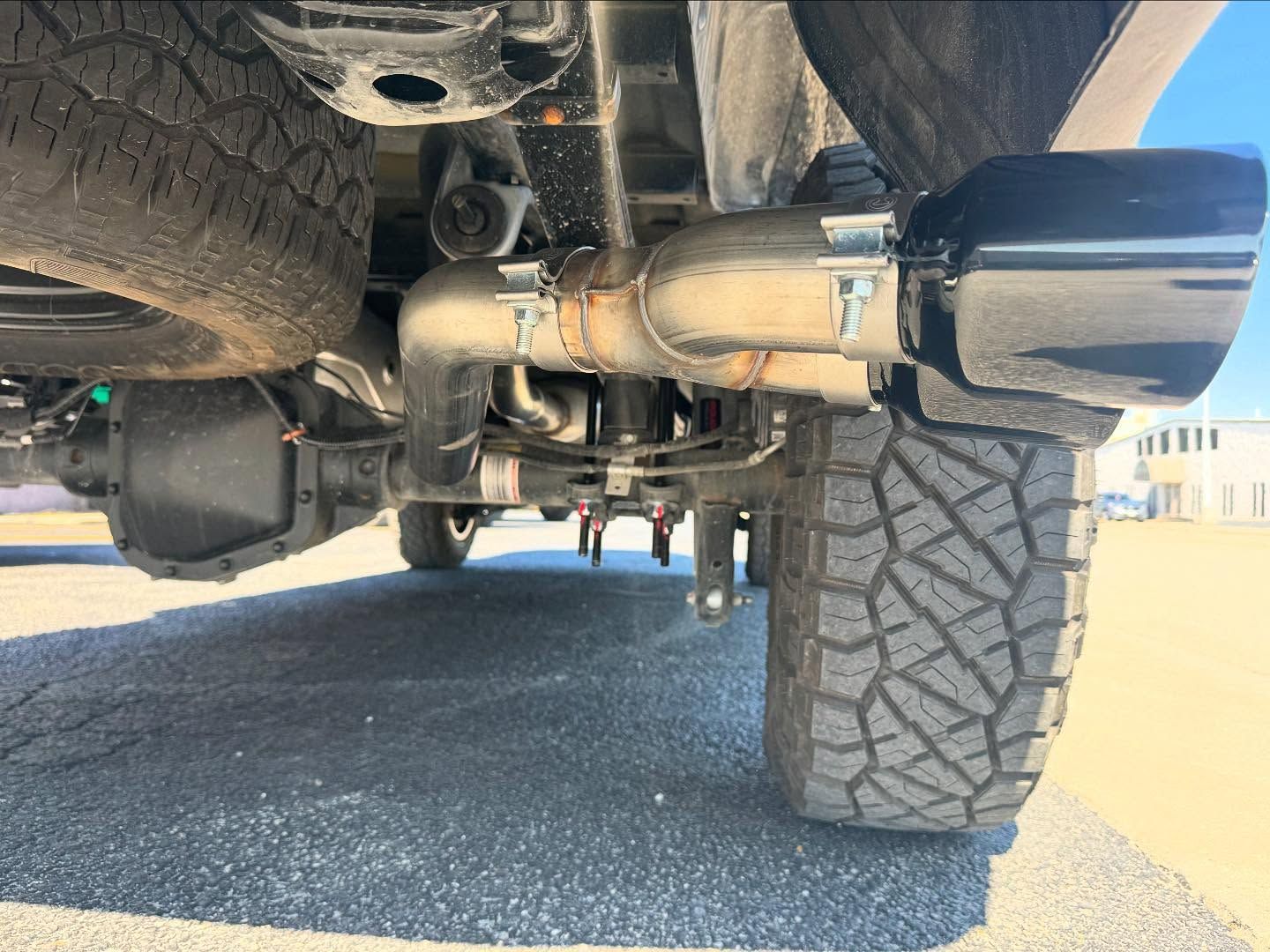 Underside view of a vehicle with off-road tires and a large exhaust system near the rear wheel
