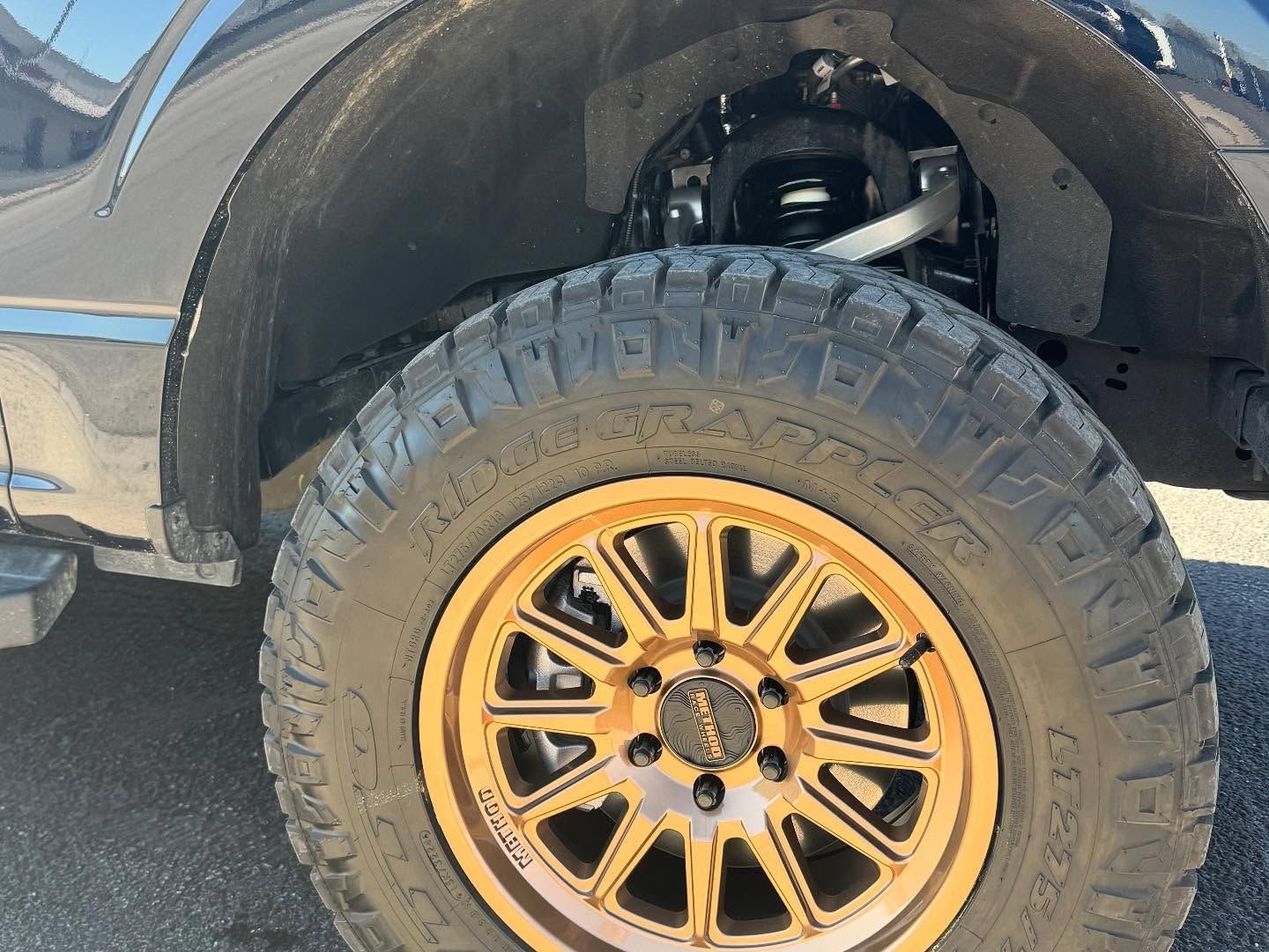 Black truck with oversized off-road tire and gold rim parked on pavement