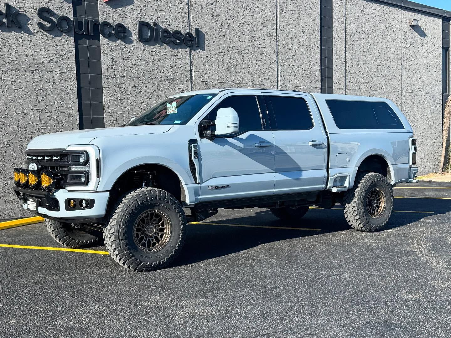 White lifted pickup truck parked outside a building with black lettering, on a sunny day