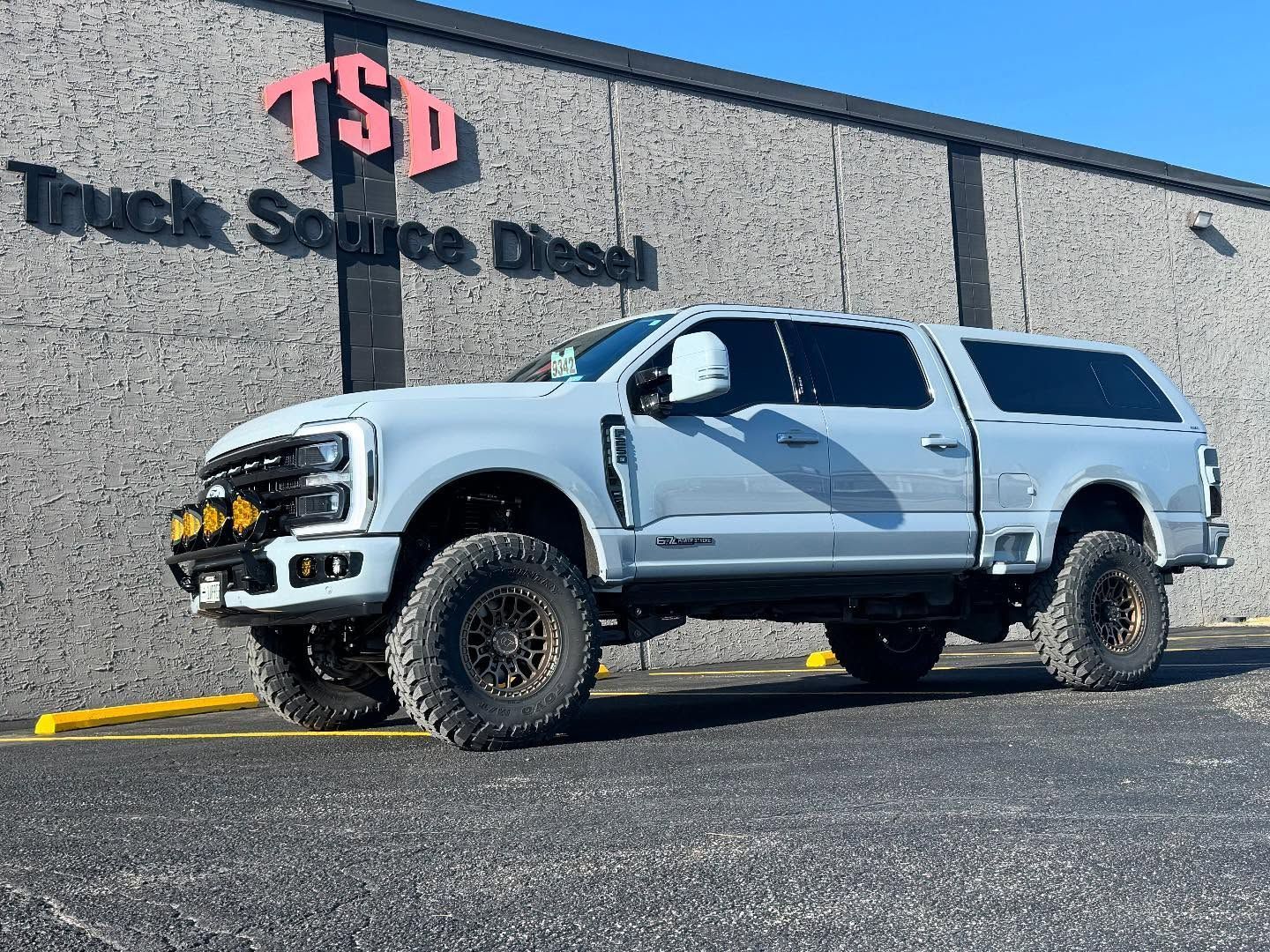 White lifted pickup truck parked outside TSD Truck & Jeep Shop, on a gravel lot.