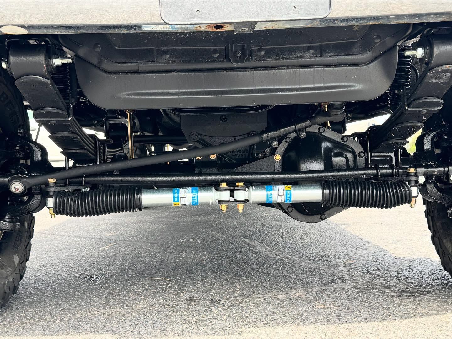 Undercarriage of a lifted vehicle showing suspension and steering components from the front