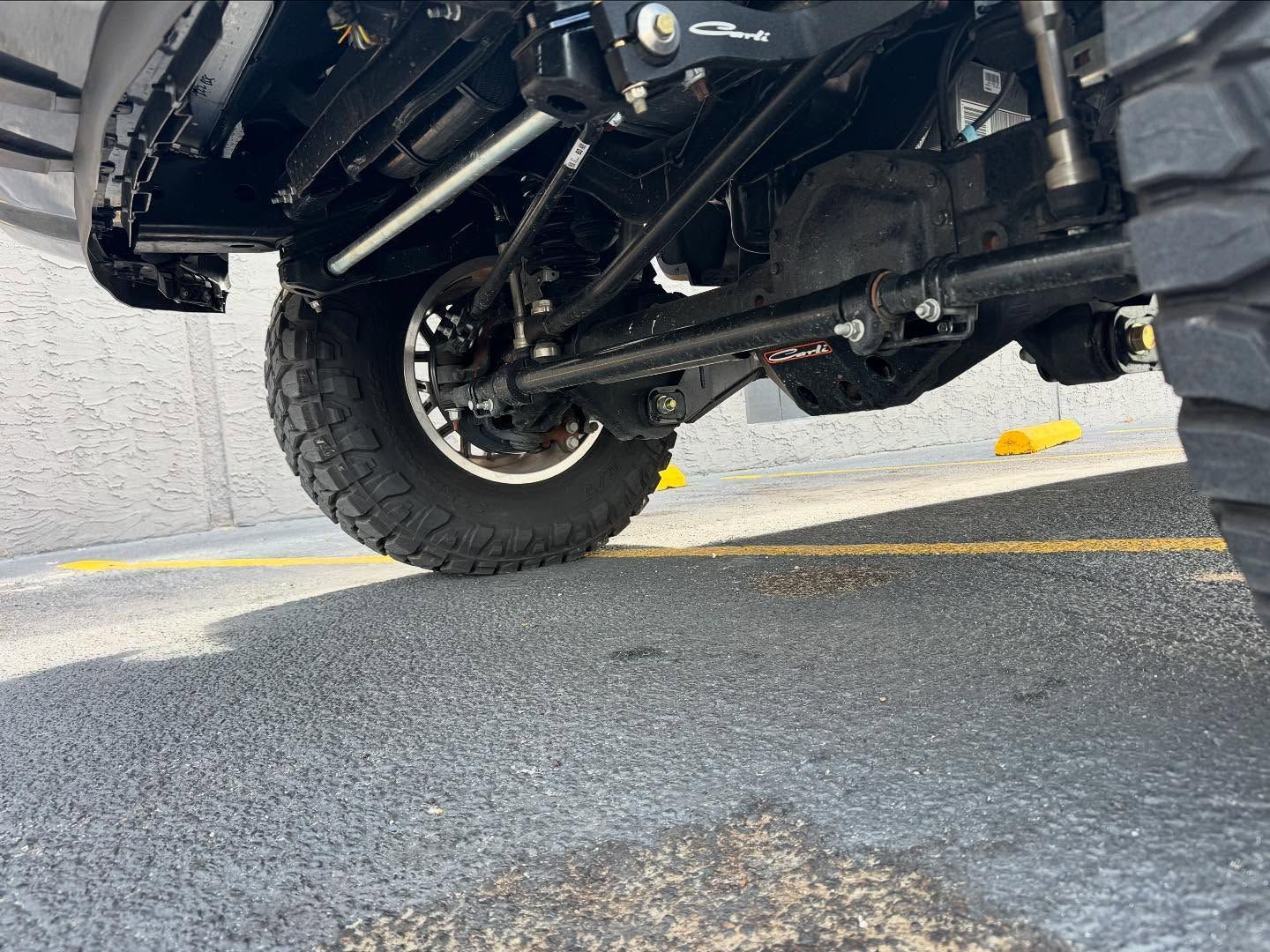 Underbody view of a black off-road vehicle with large tire on a parking lot surface