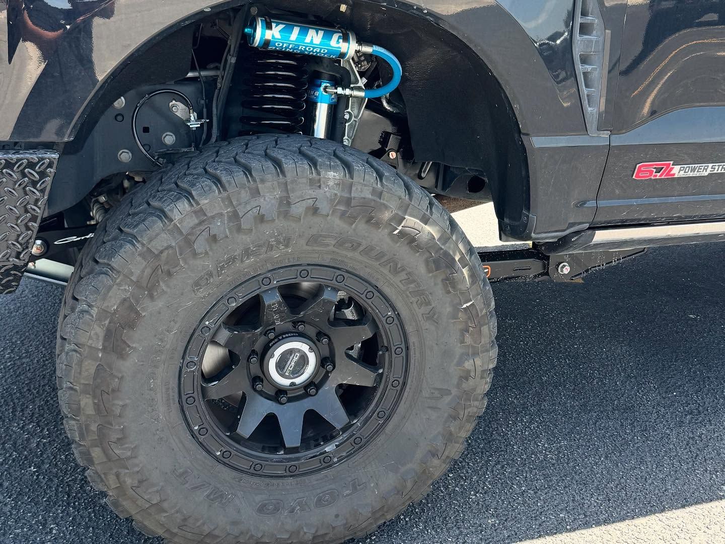 Close-up of a lifted off-road truck’s front wheel and suspension on pavement