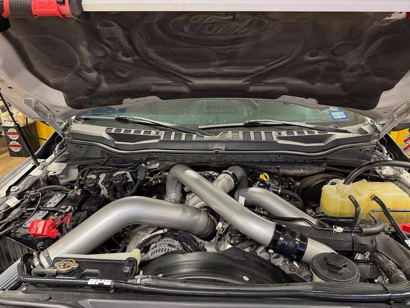 Car engine bay with large silver intake pipes and black components under an open hood