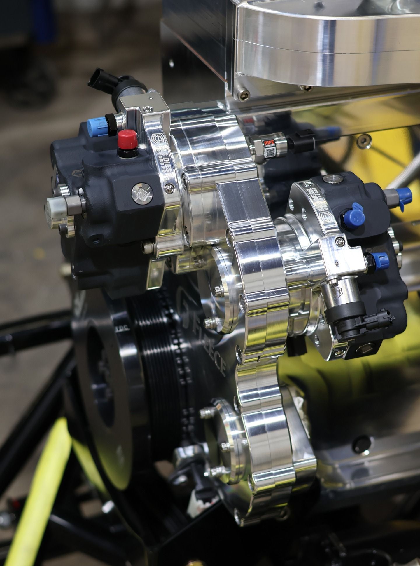 Close-up of a chrome chain mechanism with black actuators and yellow hoses on industrial equipment