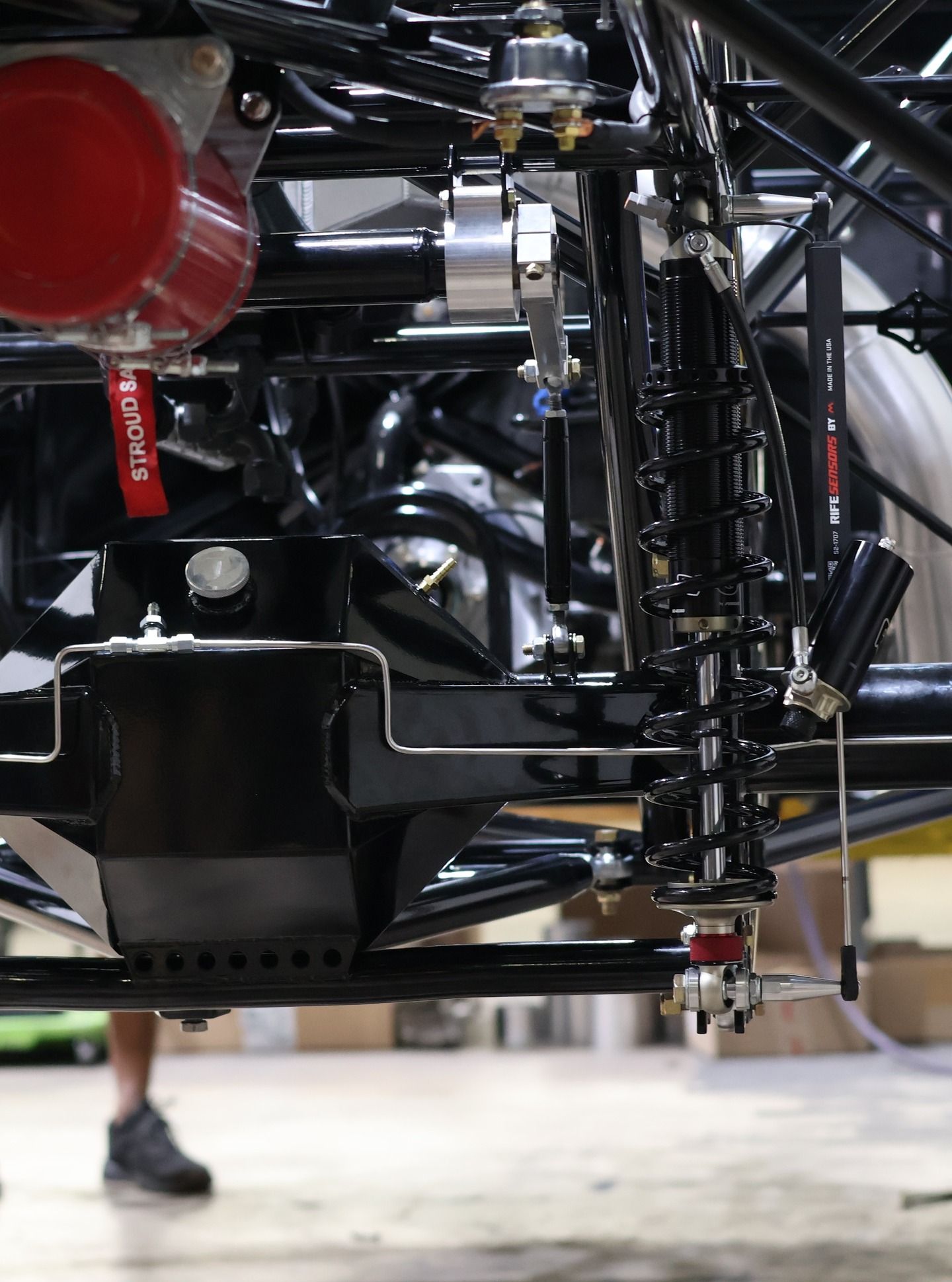 Close-up of a vehicle’s black suspension and undercarriage with red and silver components in a workshop