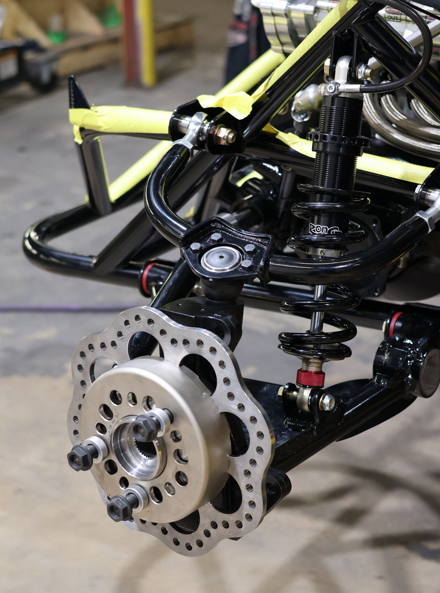 Close-up of a go-kart front wheel hub and suspension with exposed brake rotor and black chassis frame