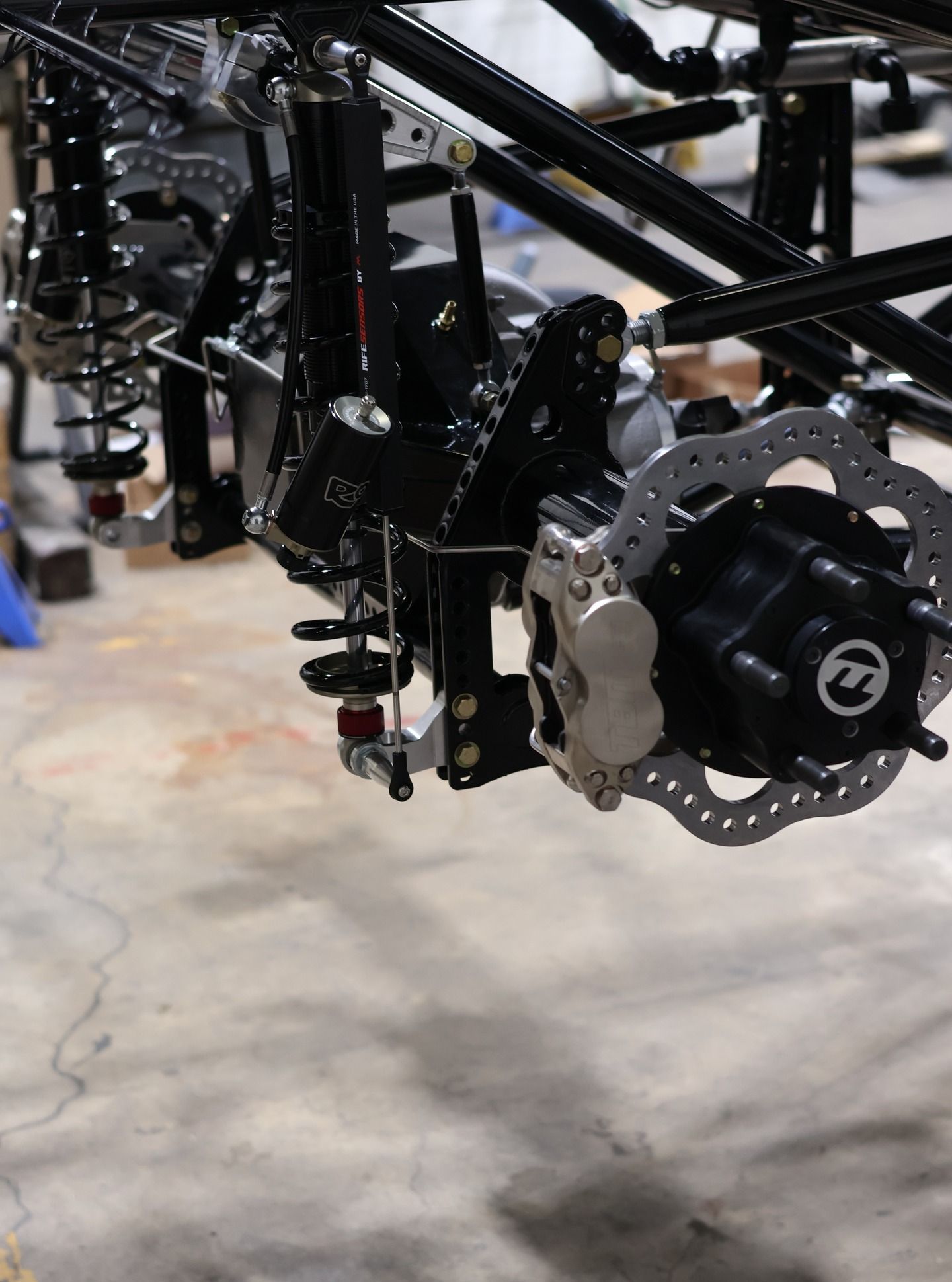 Close-up of a black off-road vehicle suspension and wheel assembly on a concrete floor