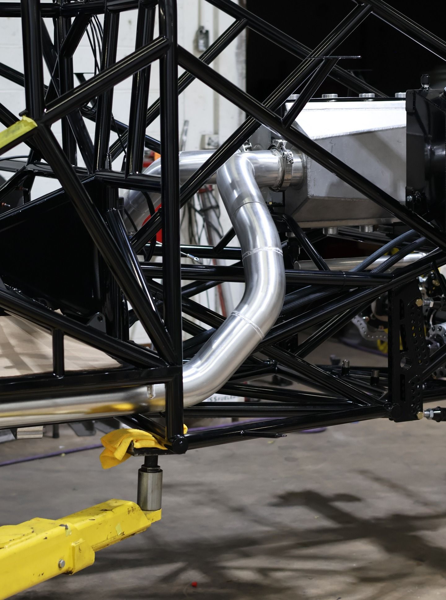 Yellow tow bar attached to a black vehicle frame with exposed silver piping in a workshop.