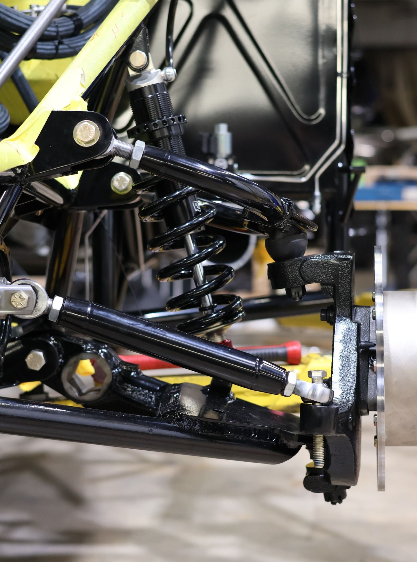 Close-up of a race car’s front suspension and wheel assembly with black metal components and yellow accents