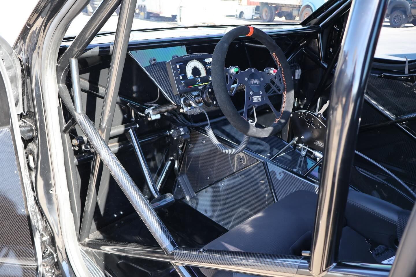 Racing car interior with roll cage, steering wheel, and carbon-fiber dashboard