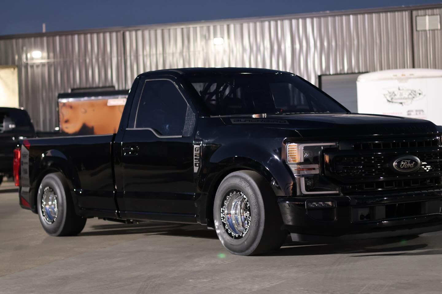 Black Ford pickup truck parked outside a warehouse at night