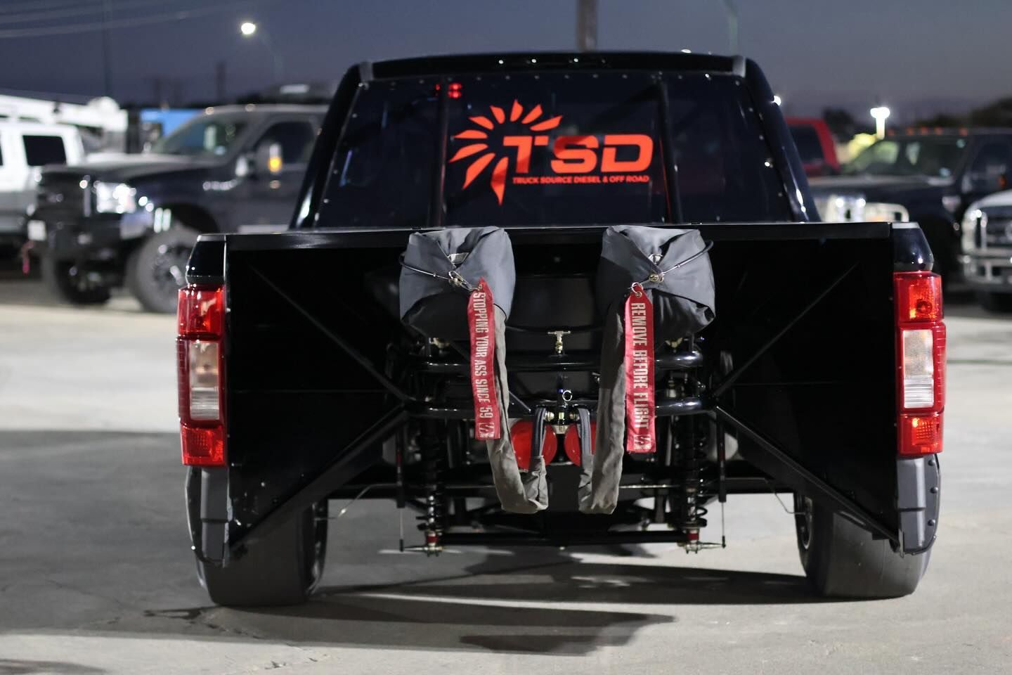 Black pickup truck with a rear-mounted drag setup and red lighting decals in a parking lot at night