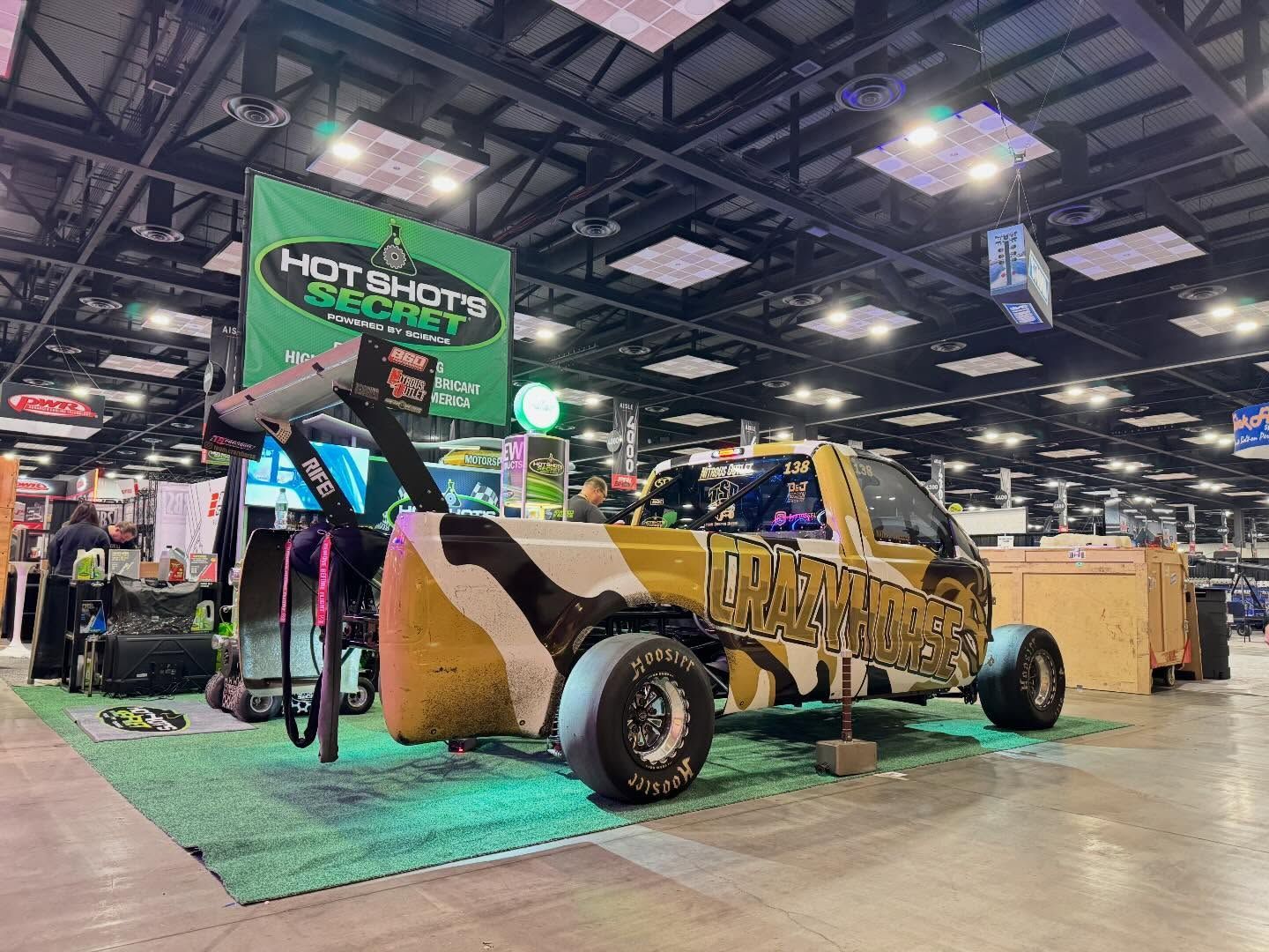Yellow off-road buggy on display at an indoor auto show with green Hoonigan sign and lighting rigs above