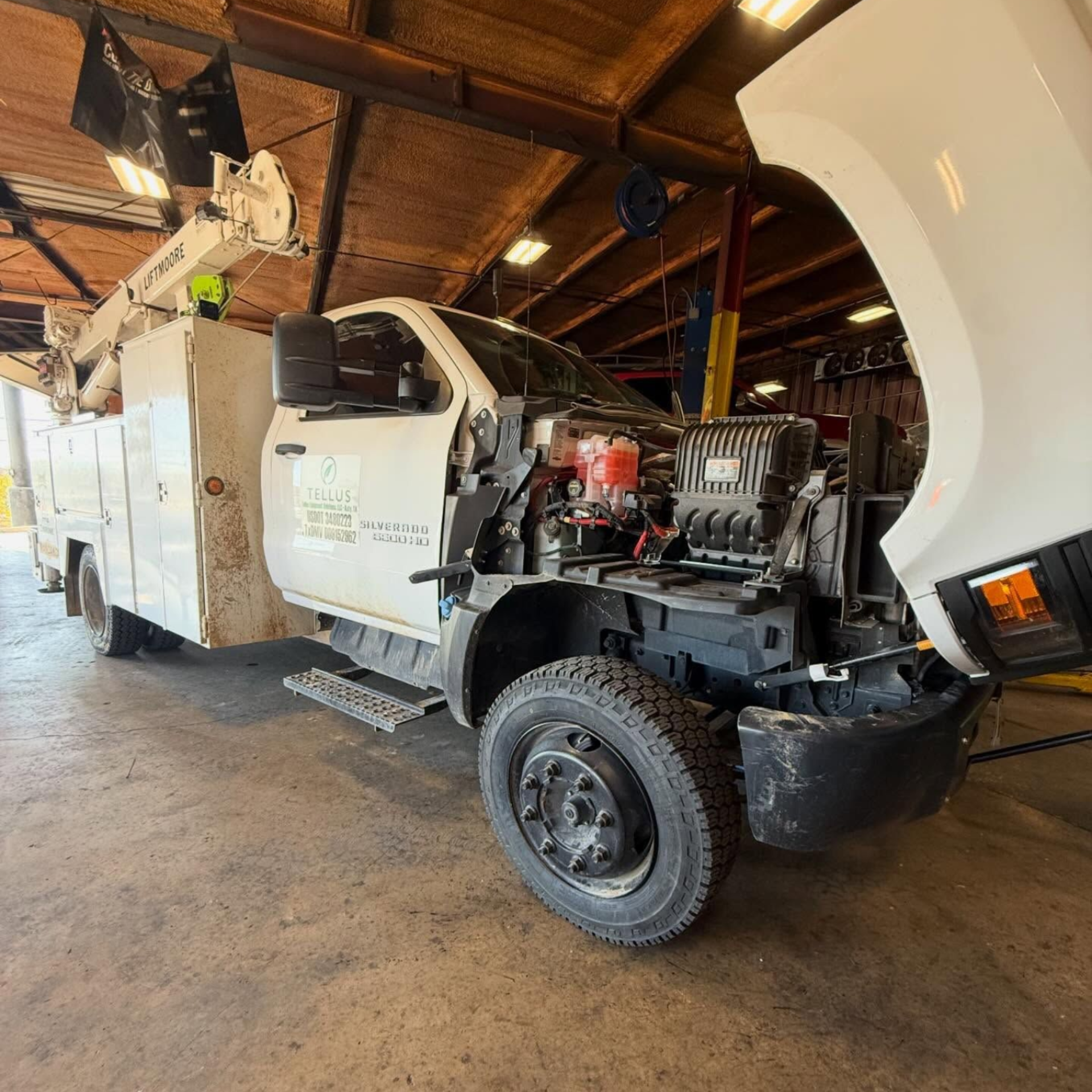 White utility truck with a boom lift parked inside a the TSD shop, front hood open.