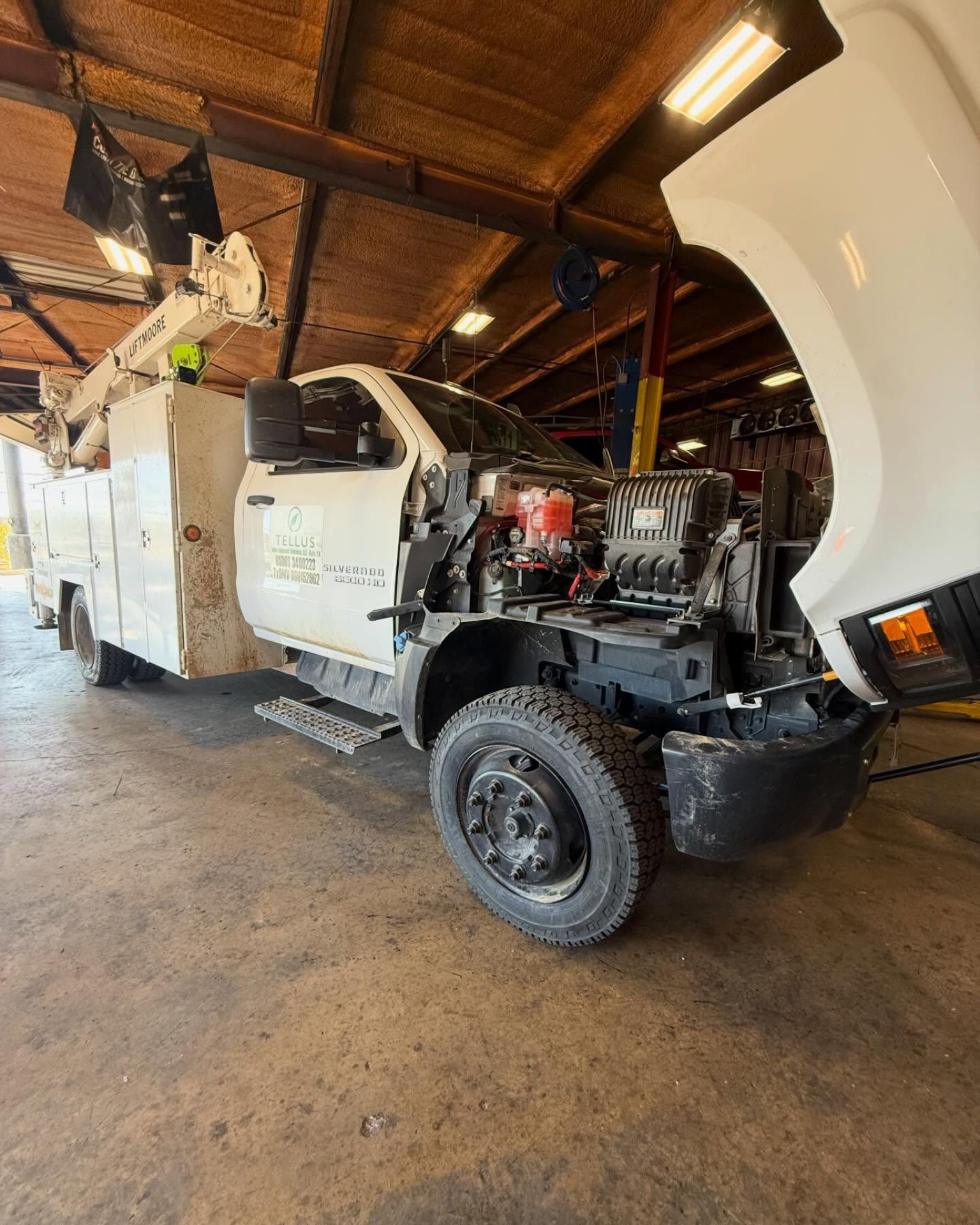 White utility truck in a garage with its hood open and engine exposed.
