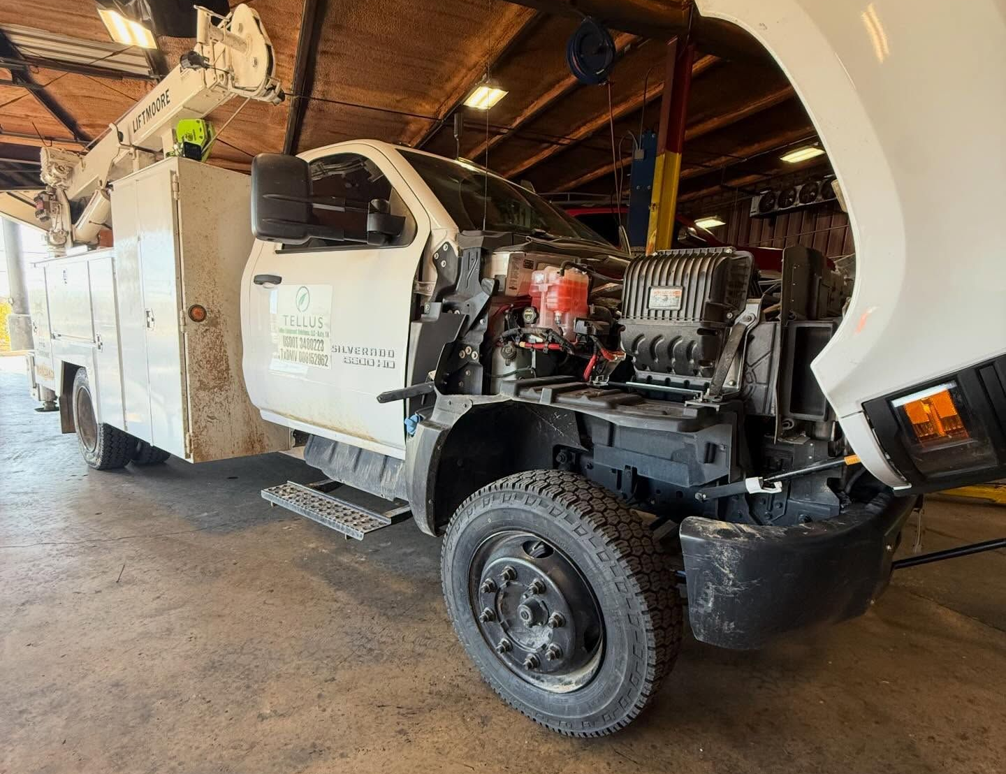 Utility truck with open engine compartment inside a garage, showing front wheel and work equipment.