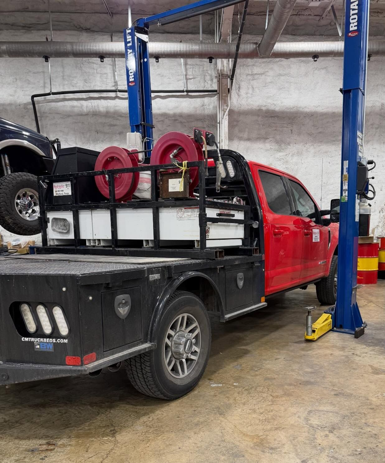 Red pickup truck on a lift in an auto repair shop, with equipment in the bed.