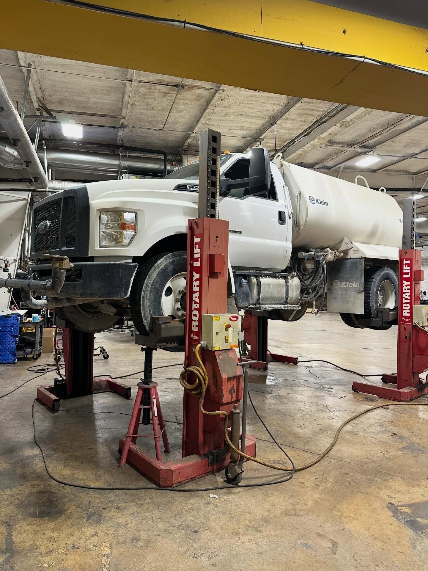 White truck lifted on red shop jacks inside an auto repair garage