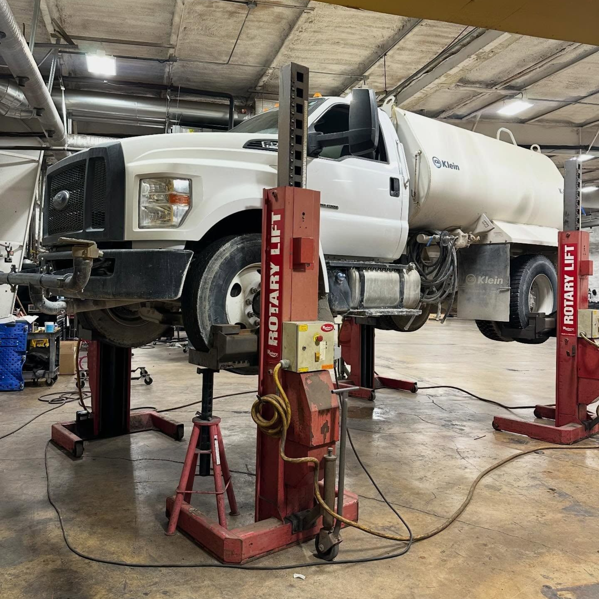 White service truck lifted on red hydraulic shop lifts inside a garage.
