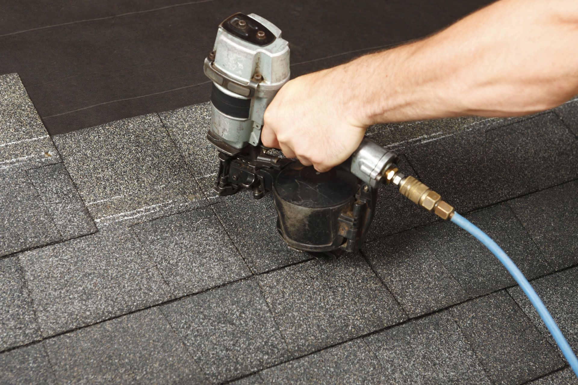 Person using a nail gun to install asphalt roof shingles.