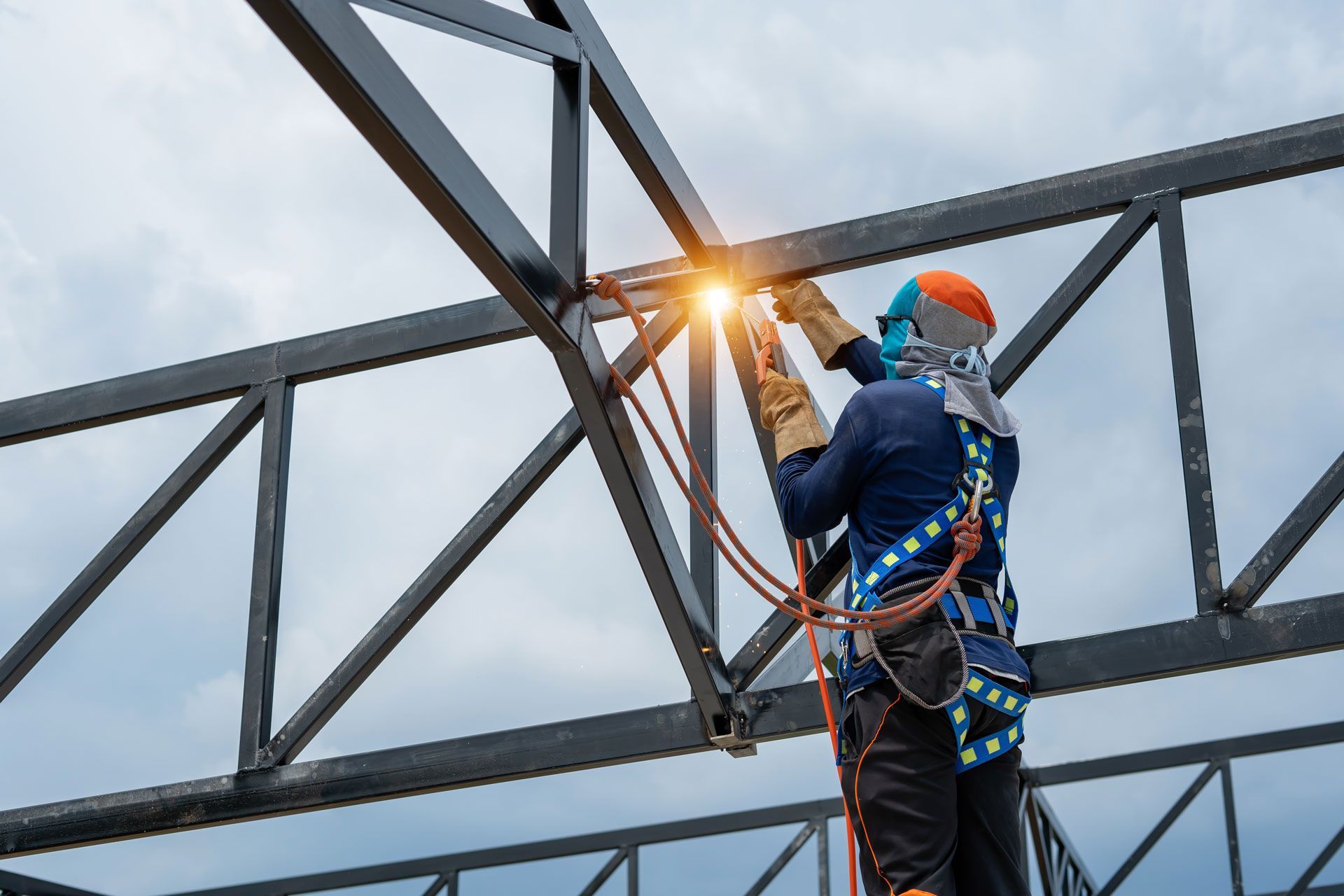 Welder in safety gear working on metal beams outdoors, sparks flying.